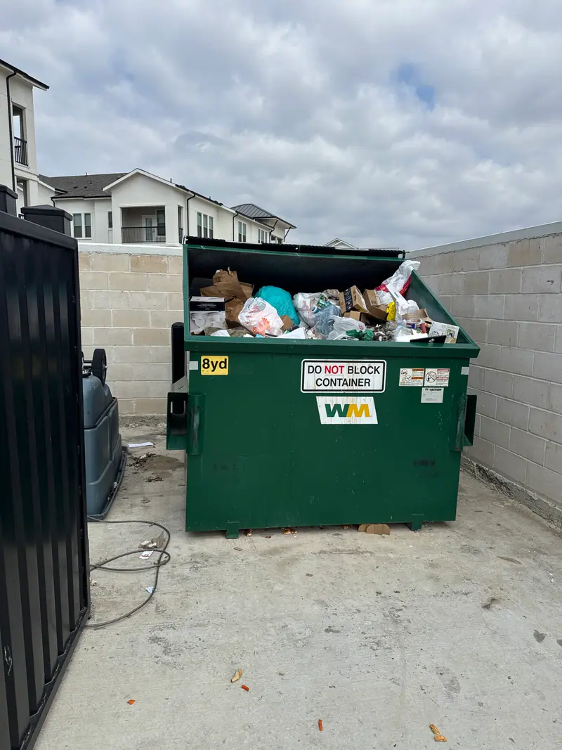 Overflowing eight yard dumpster at an apartment trash enclosure