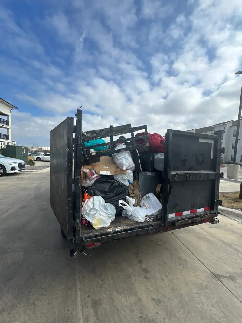 Dump trailer loaded with bagged trash and bulk items at an apartment complex