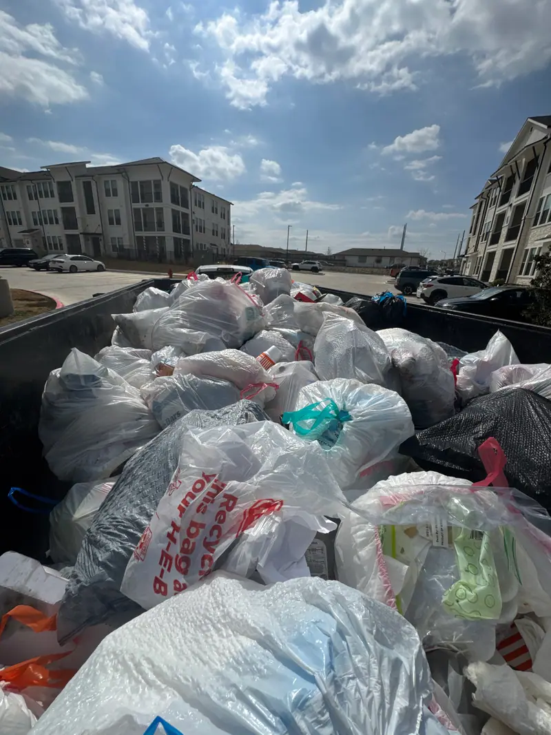 Trailer bed full of bagged household trash with apartment buildings behind