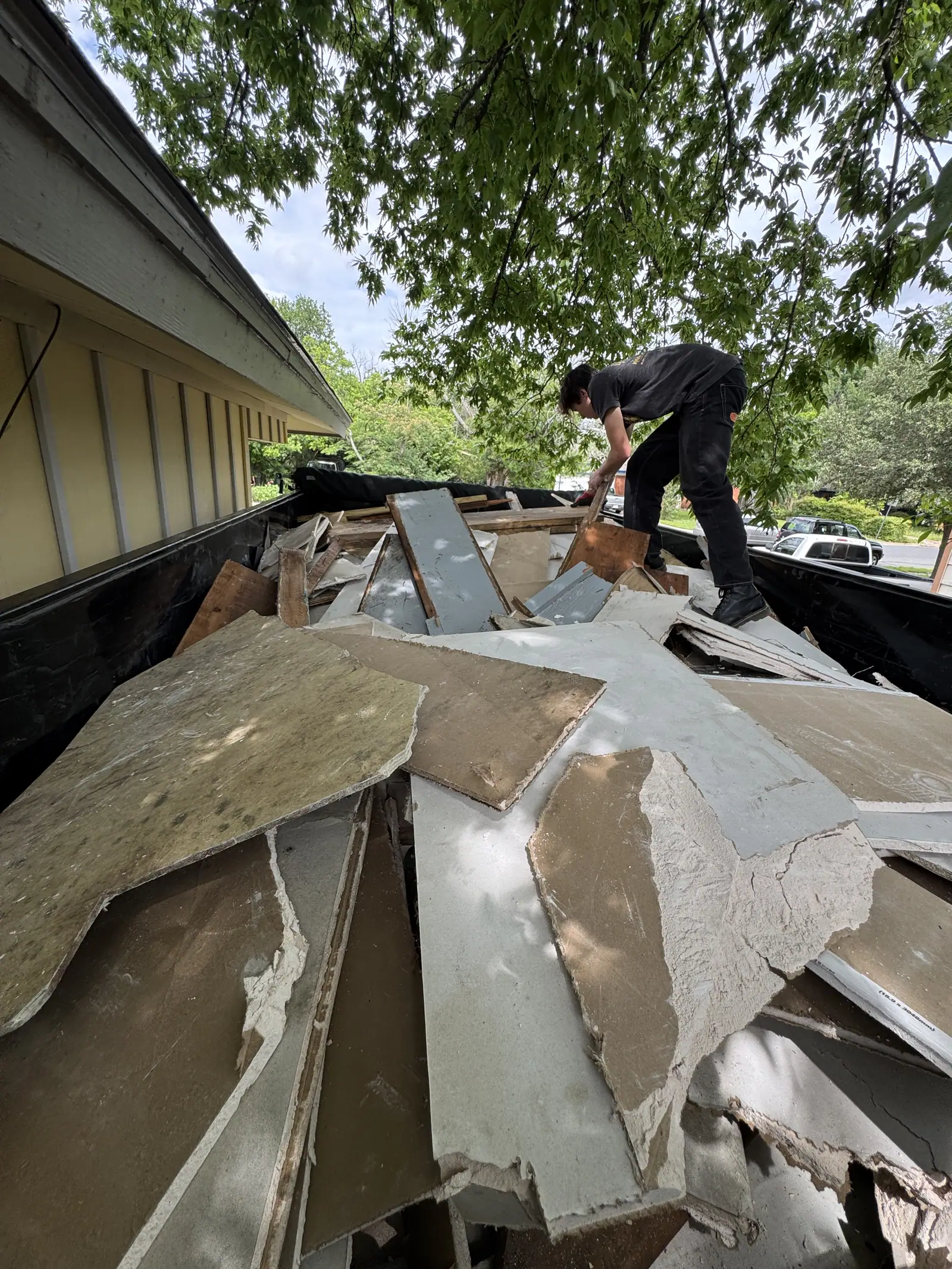 Elite Demo and Junk Removal crew member standing in the dump trailer stacking torn out siding and debris at an Austin house