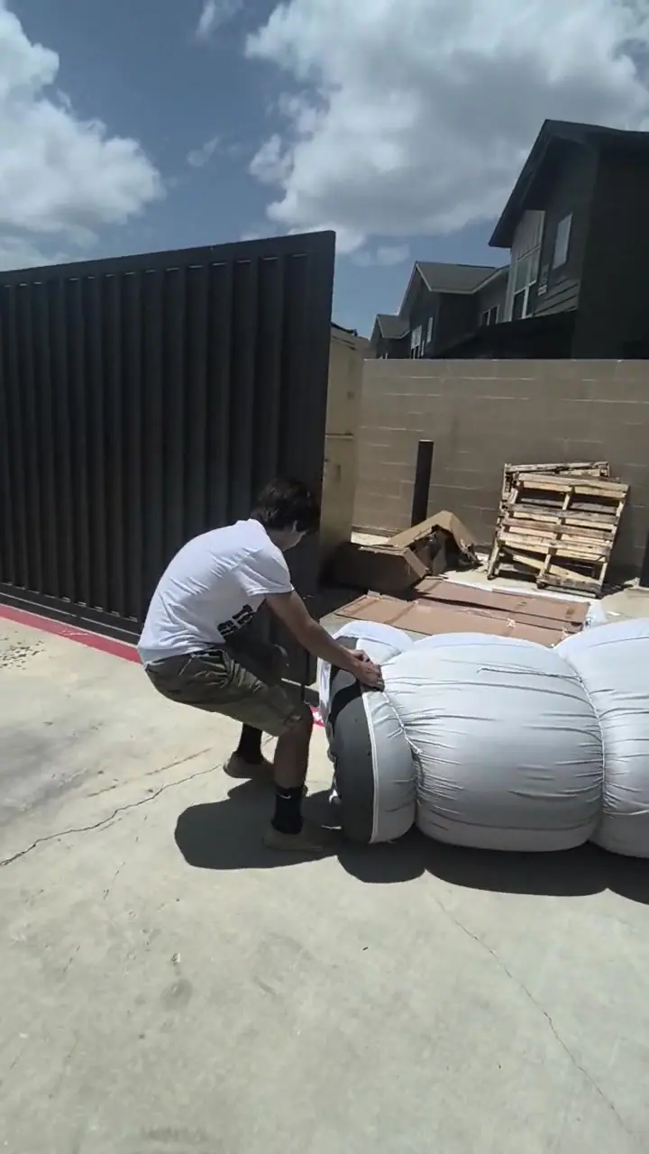 Crew member rolling a wrapped mattress out of the apartment trash enclosure toward the dump trailer