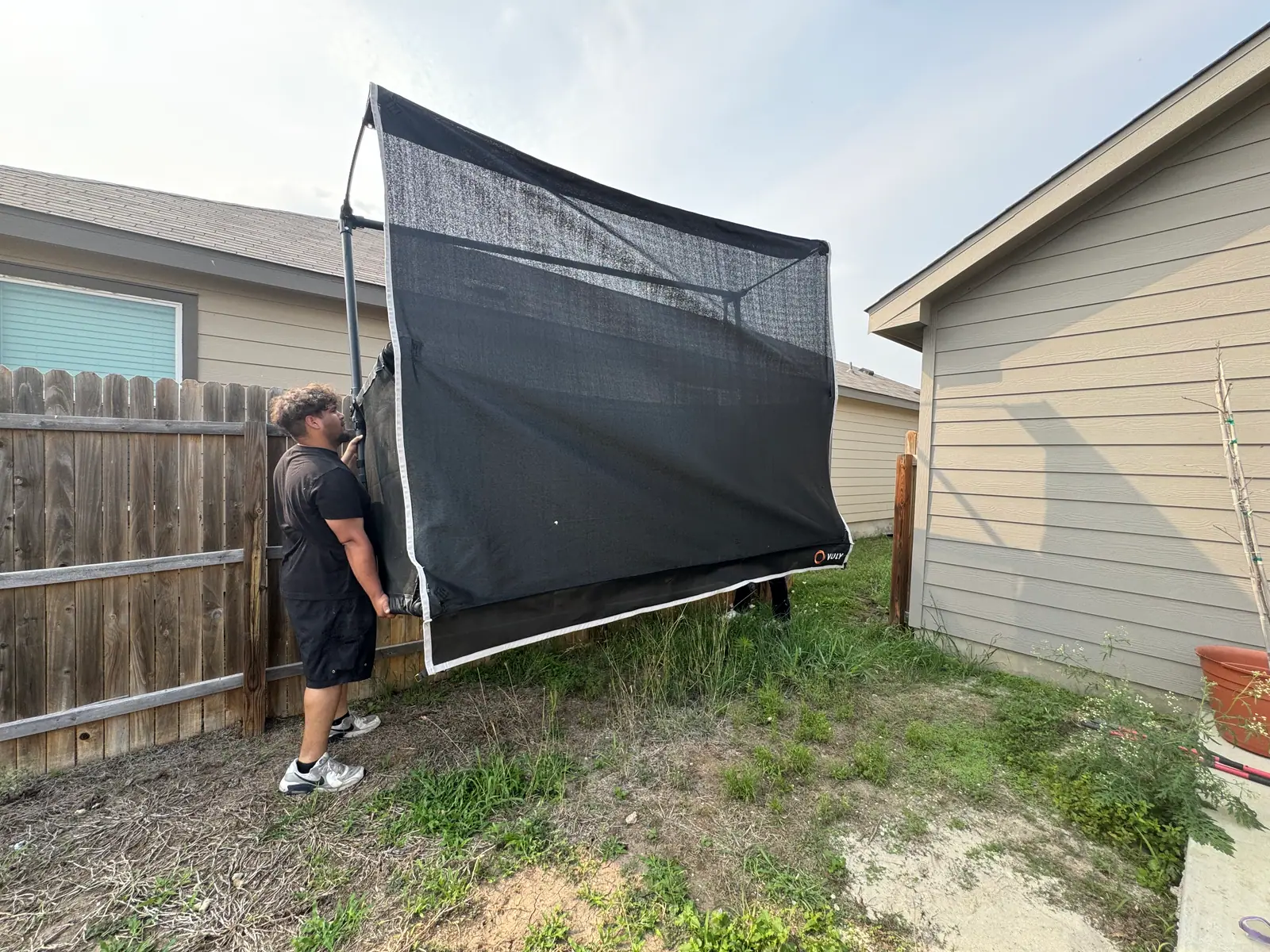 Crew member carrying a trampoline net and frame out through the side yard in San Antonio
