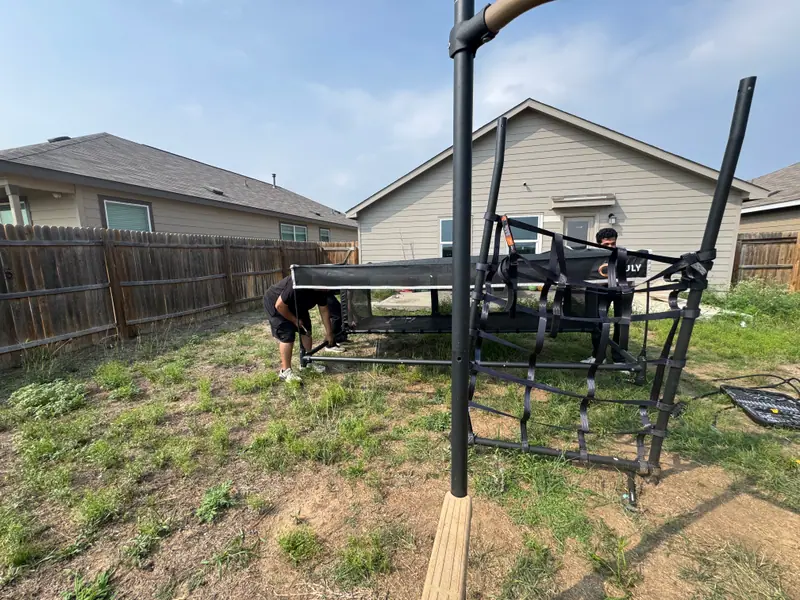 Two crew members dismantling a large backyard trampoline in San Antonio