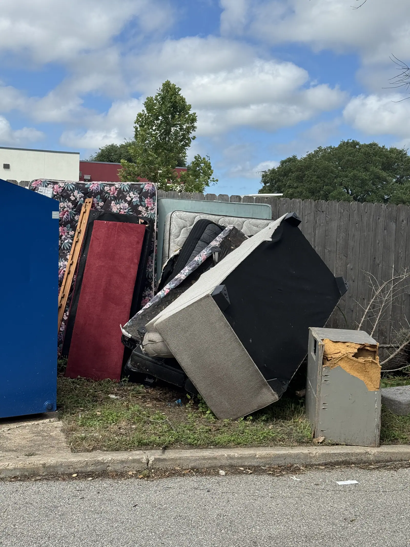Mattresses, box springs and a box spring frame stacked beside the dumpster at a San Marcos apartment community
