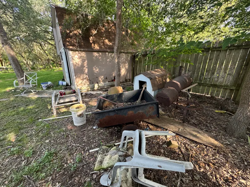 Backyard junk pile in San Marcos with a dog house, metal feed trough and lawn chairs
