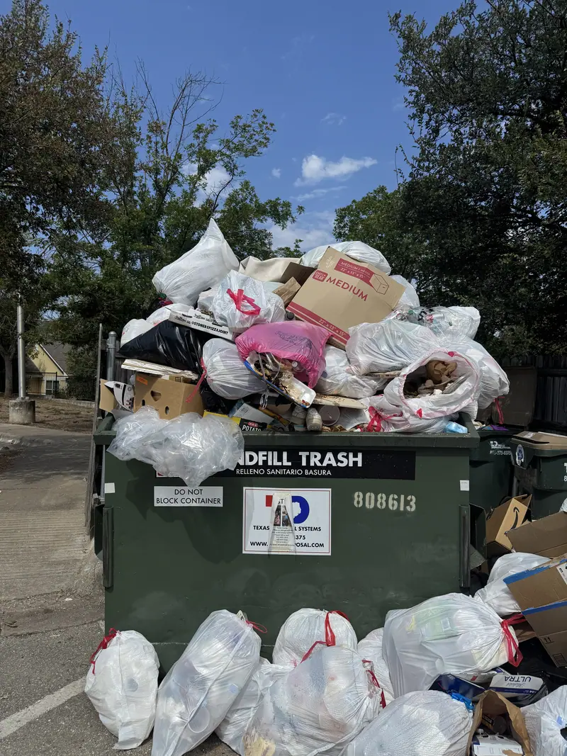 Overflowing landfill trash dumpster at a San Marcos property buried under bagged trash and boxes