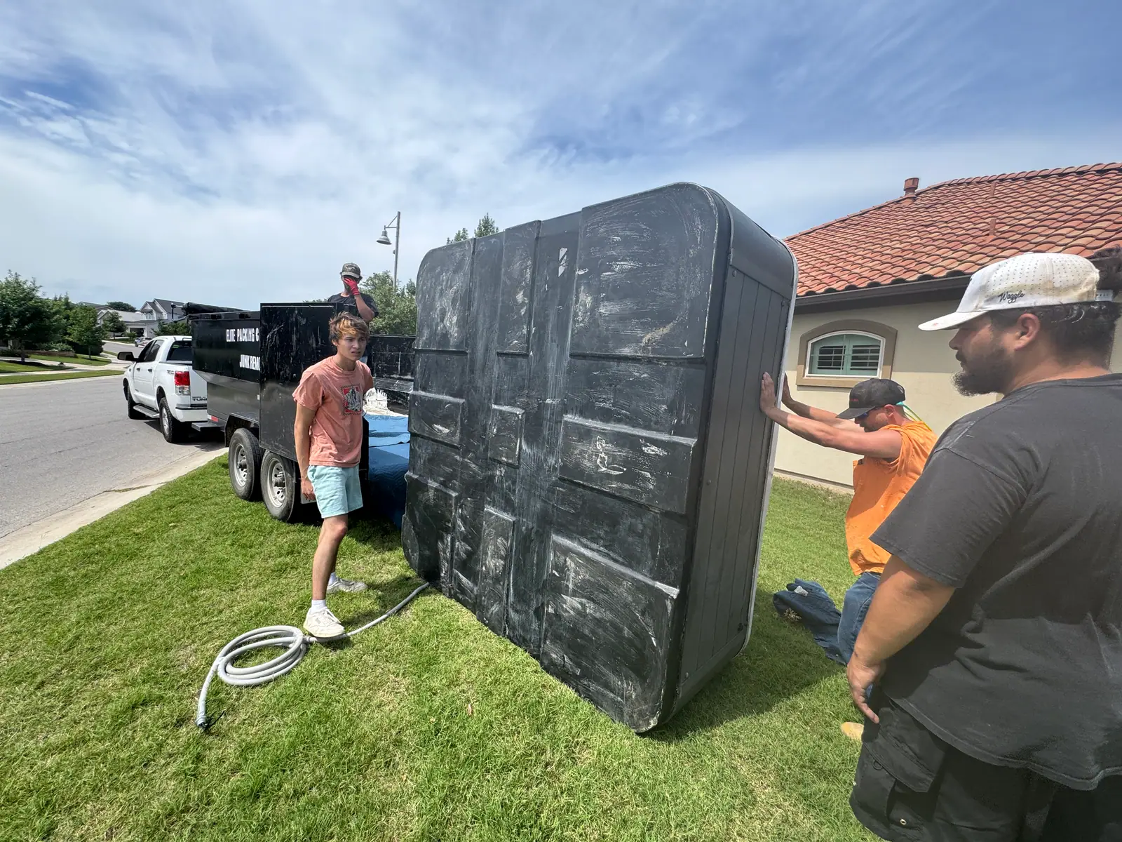 Elite Demo and Junk Removal crew standing a hot tub shell upright beside the company dump trailer in San Marcos